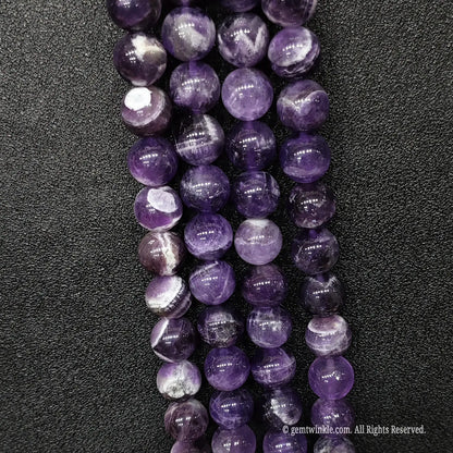 Parallel rows of genuine chevron dream amethyst crystal beads in four to twelve millimeter sizes displaying sharp white patterns