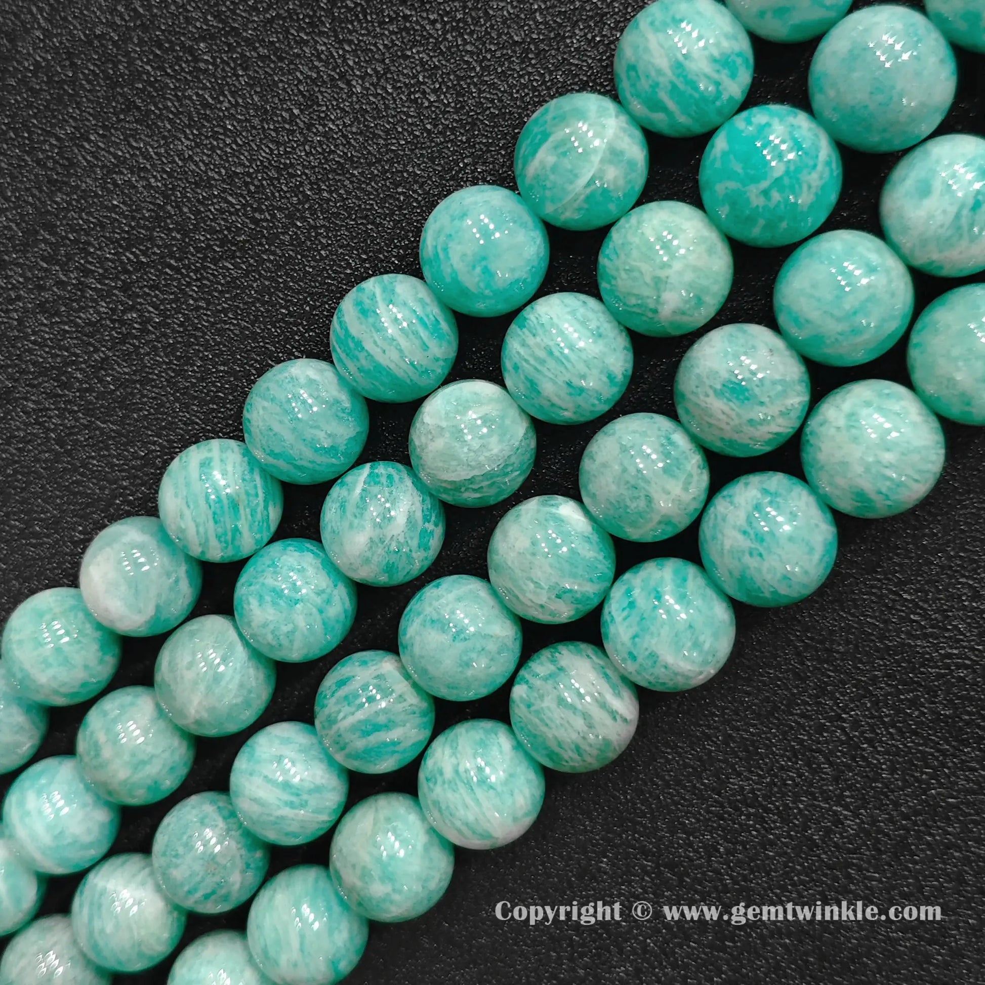 Parallel strands of chunky natural Grade B amazonite large round beads on dark surface