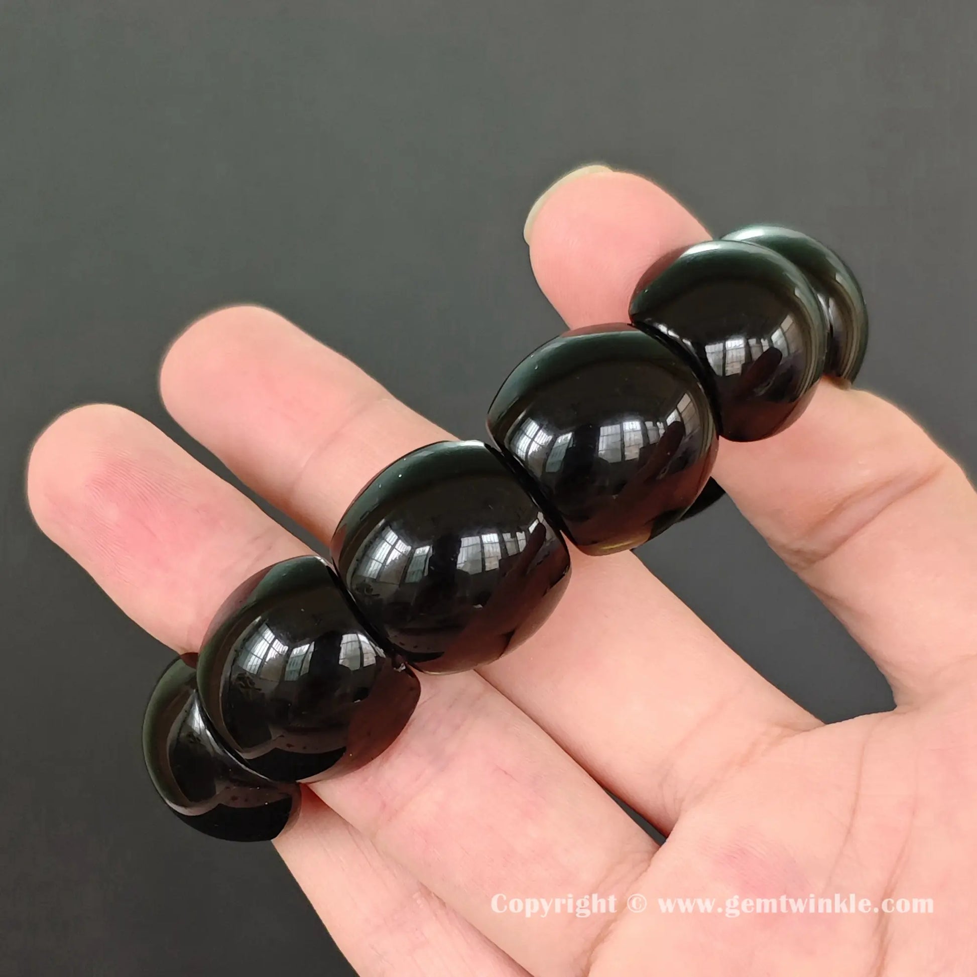side view of natural black obsidian stretch cuff bracelet held by fingers highlighting machine polish