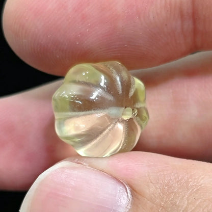Fingers holding a 12mm yellow citrine pumpkin bead showing radial grooves and center drill hole
