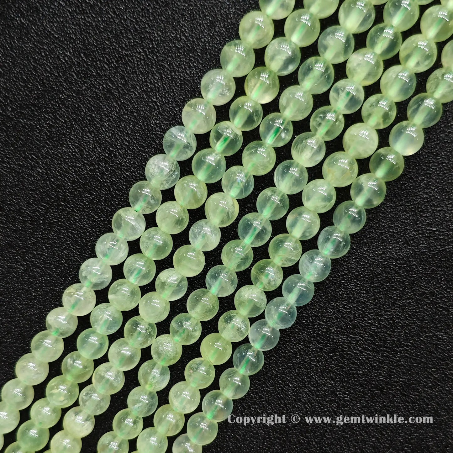 Angled view of Grade A prehnite round bead strands laid parallel on dark surface