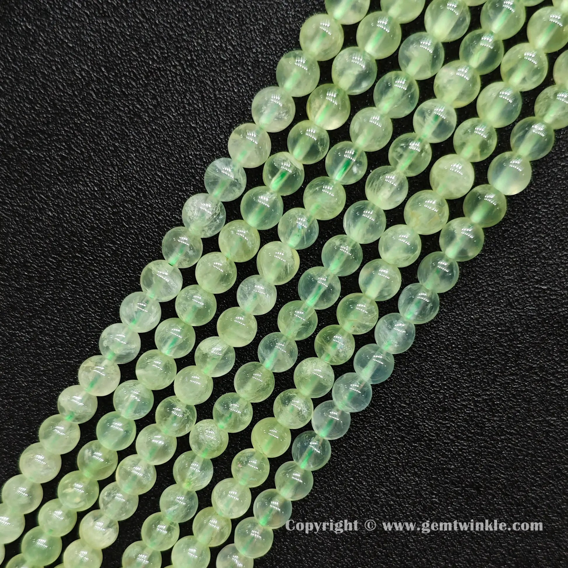 Angled view of Grade A prehnite round bead strands laid parallel on dark surface
