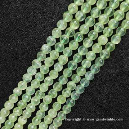 Angled view of Grade A prehnite round bead strands laid parallel on dark surface