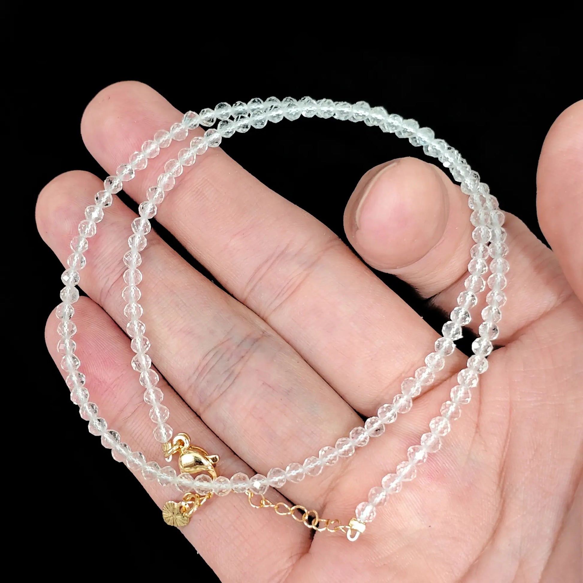clear quartz micro faceted bead strand held in hand with gold clasp
