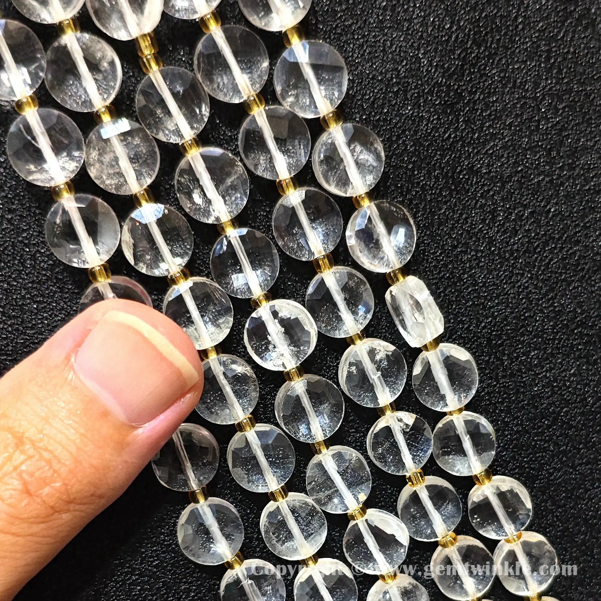 Hand holding strands of clear quartz faceted coin beads for size inspection