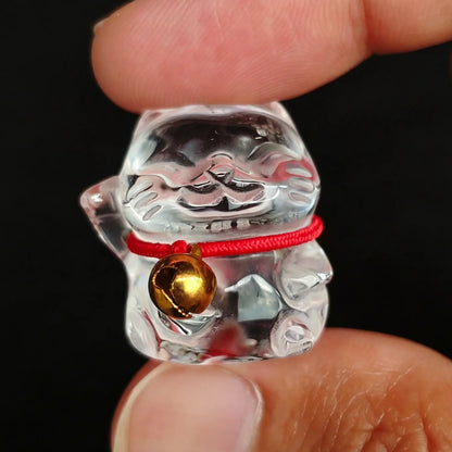 Clear quartz lucky fortune cat carving with red cord and gold bell held between fingers