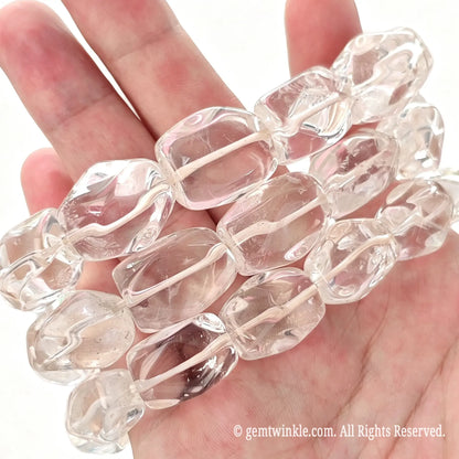 Stacked clear quartz large freeform nugget stretch bracelets arranged across open hand showing approx 20mm bead length with internal cloud textures