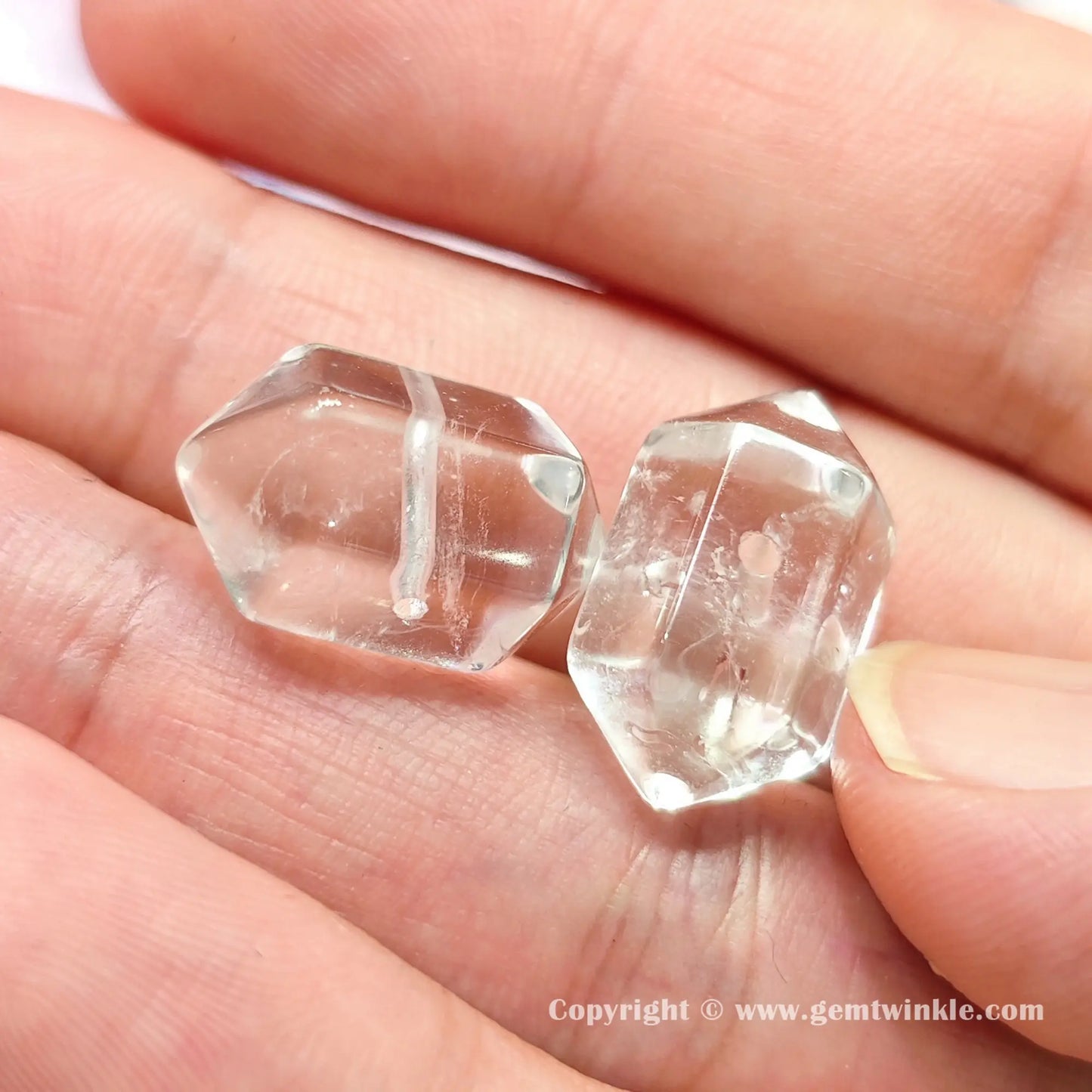 Close up details of natural clear quartz hexagonal column double point bead showing glossy surfaces on fingers