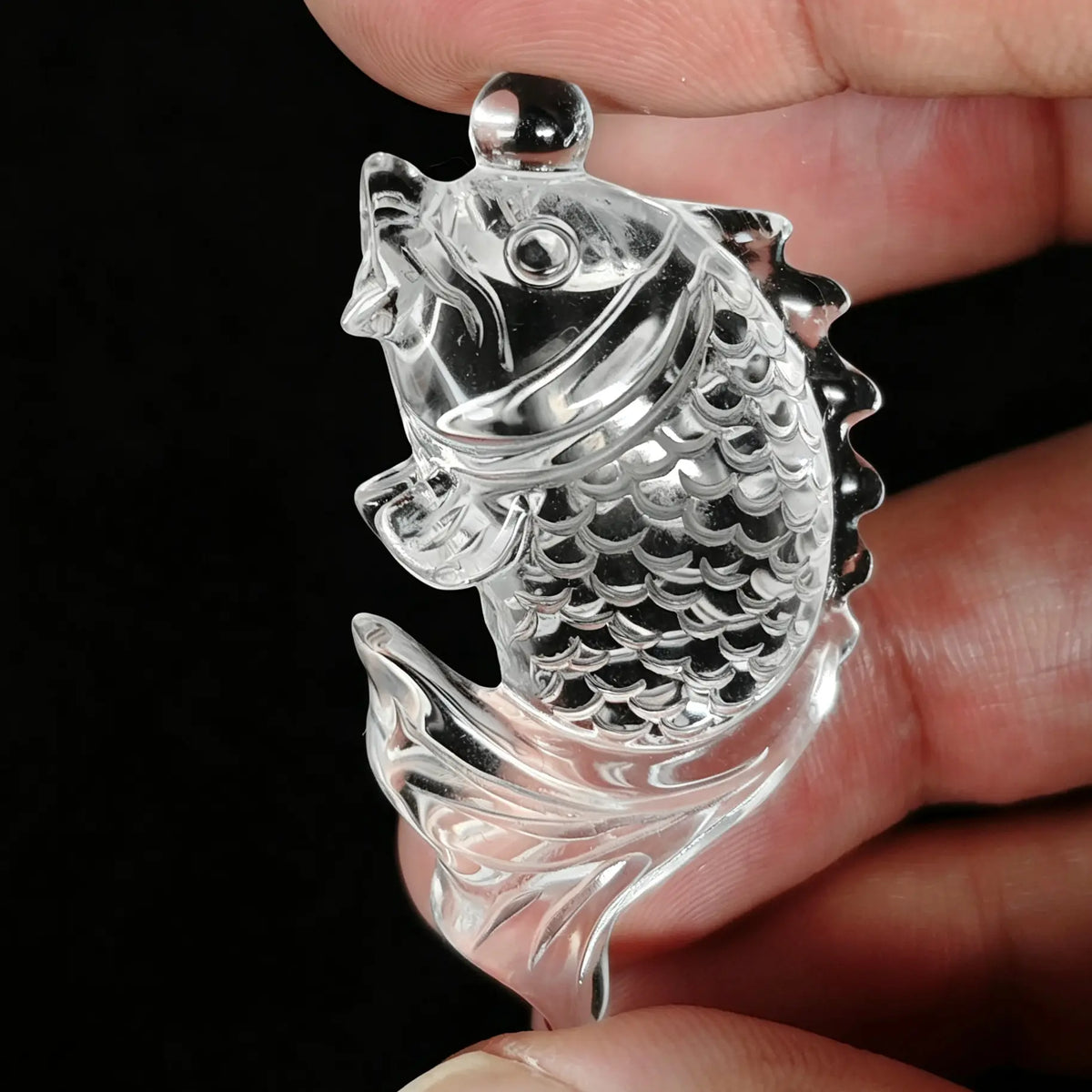 Clear quartz koi fish carving with scale reliefs held between fingers showing optical transparency