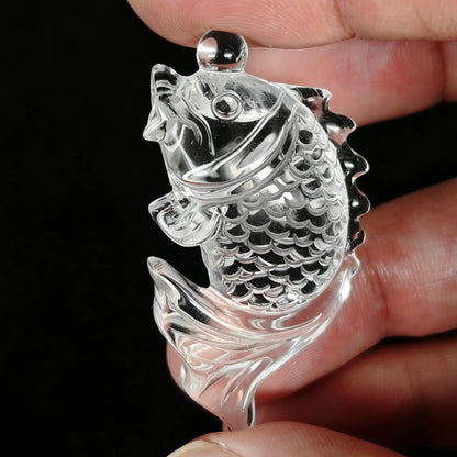 Clear quartz koi fish carving with scale reliefs held between fingers showing optical transparency