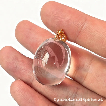 Hand preview of a ~25mm clear quartz oval pendant highlighting pristine stone clarity