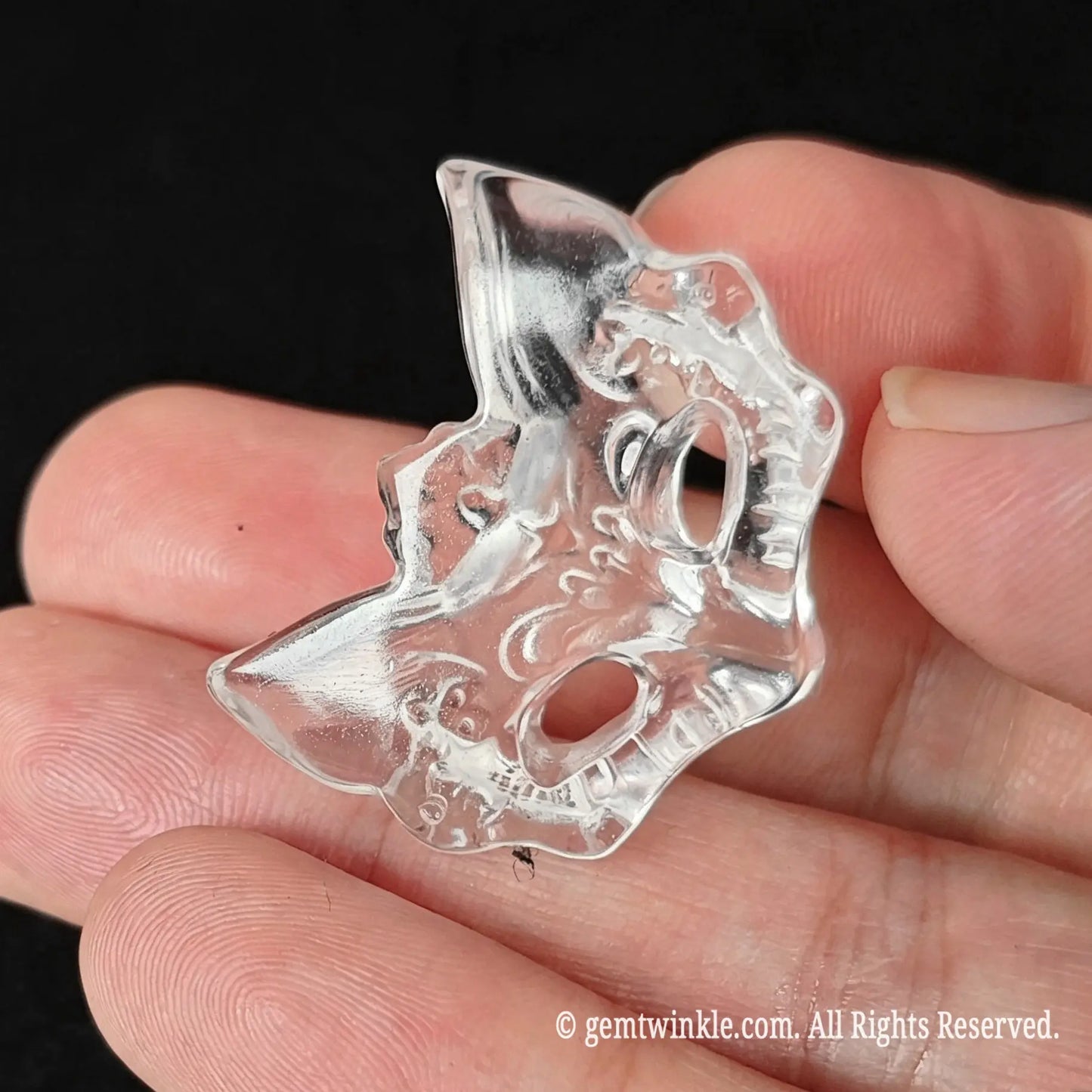 Angled view of clear quartz fox mask pendant held in hand showing hollowed eye sockets and carving relief