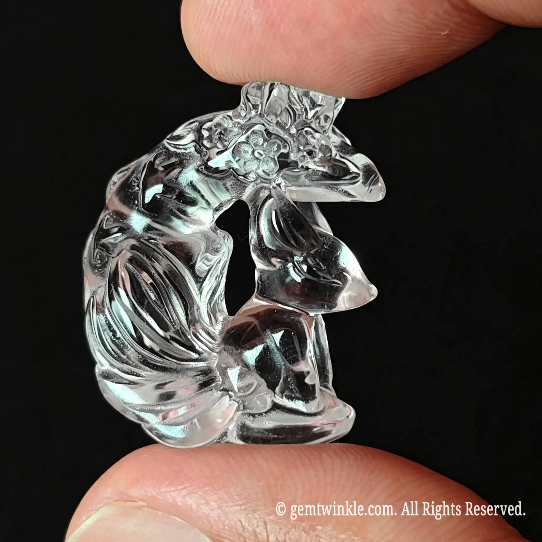 Angled view of clear quartz carved fox pendant held in hand showing 3D tail details and crystal clarity