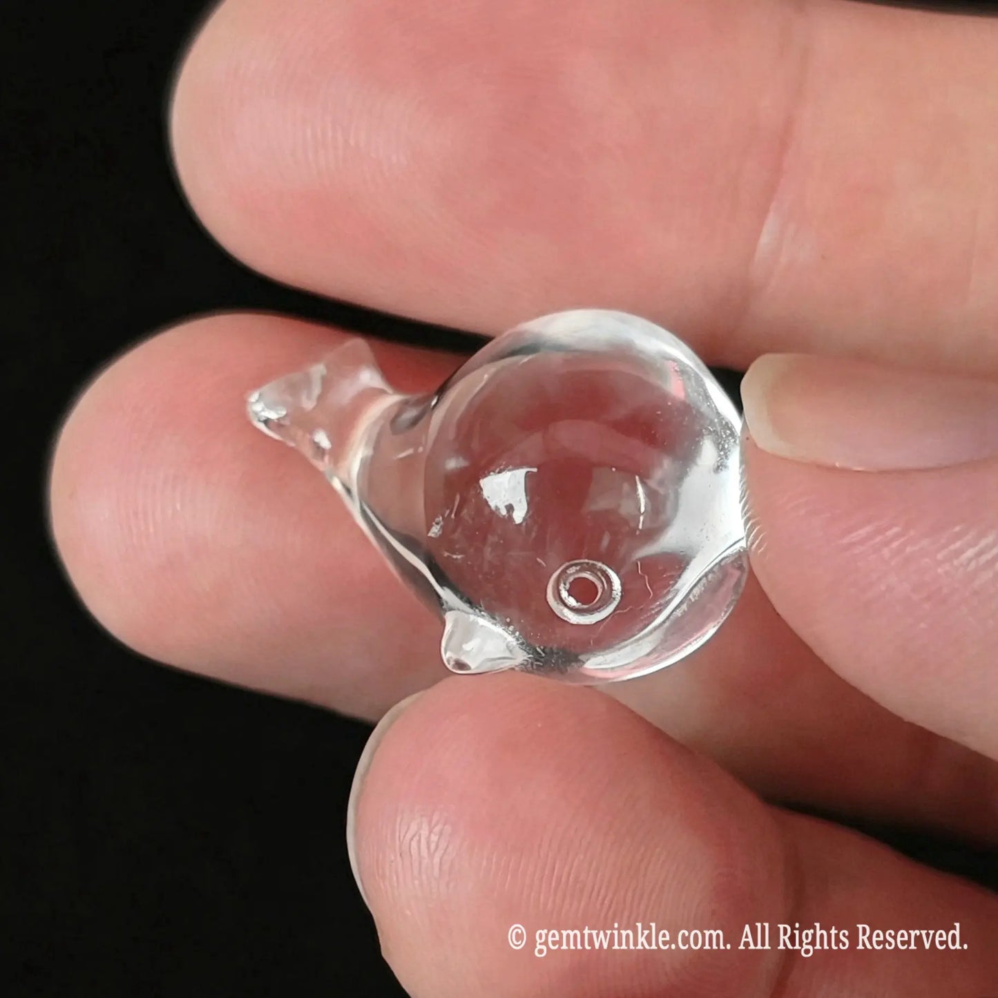Side view of 20mm clear quartz carved whale held in hand showing glass-like clarity and carved eye detail