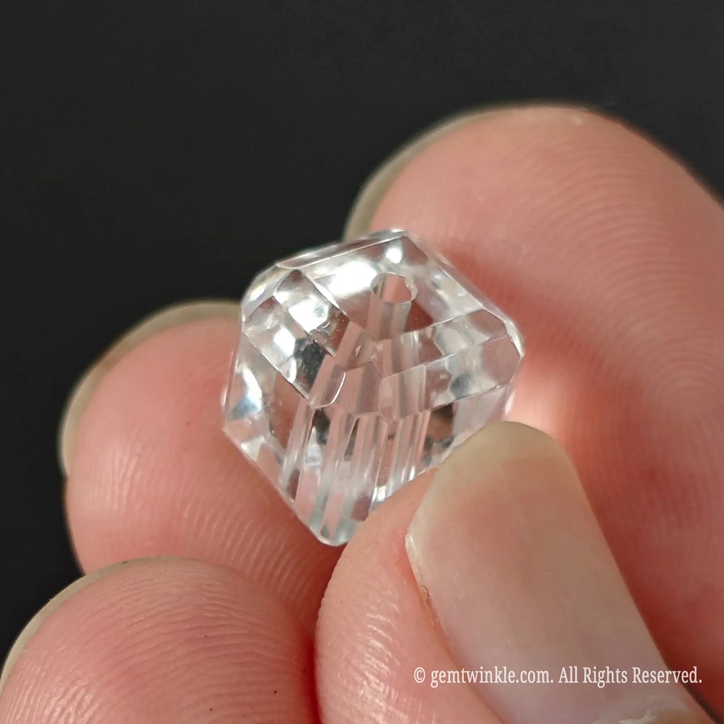 Clear quartz faceted cube bead held in fingers showing high clarity ice clean transparency and precision cut corners