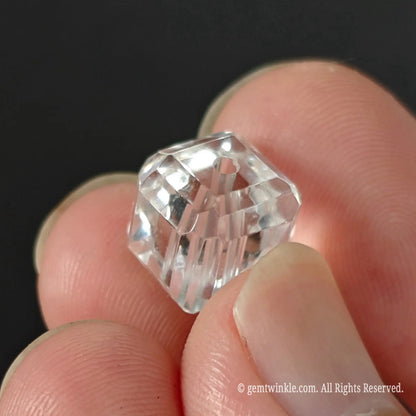 Clear quartz faceted cube bead held in fingers showing high clarity ice clean transparency and precision cut corners