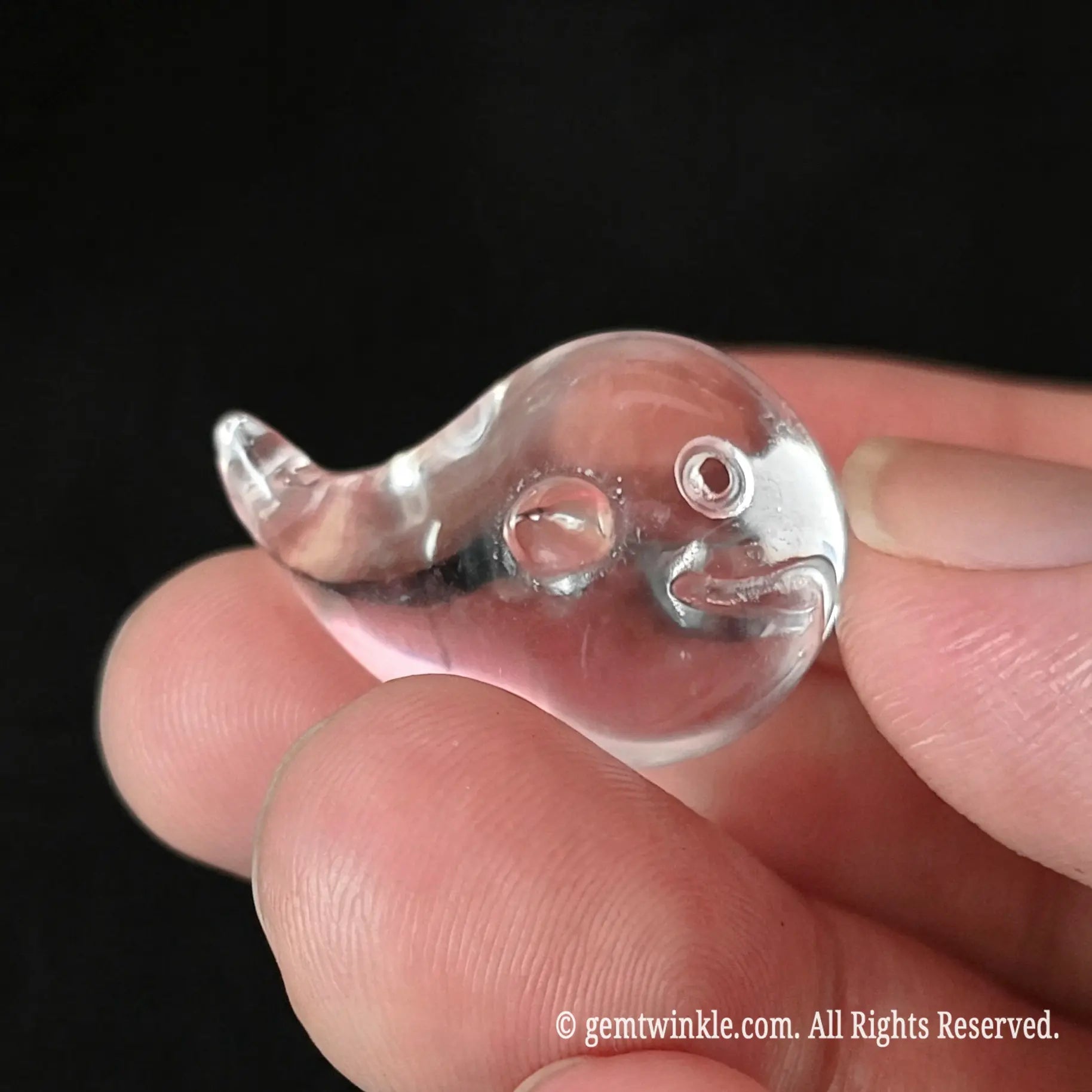 Back view of 20mm carved clear quartz mini whale held between fingers highlighting smooth edges and light reflection