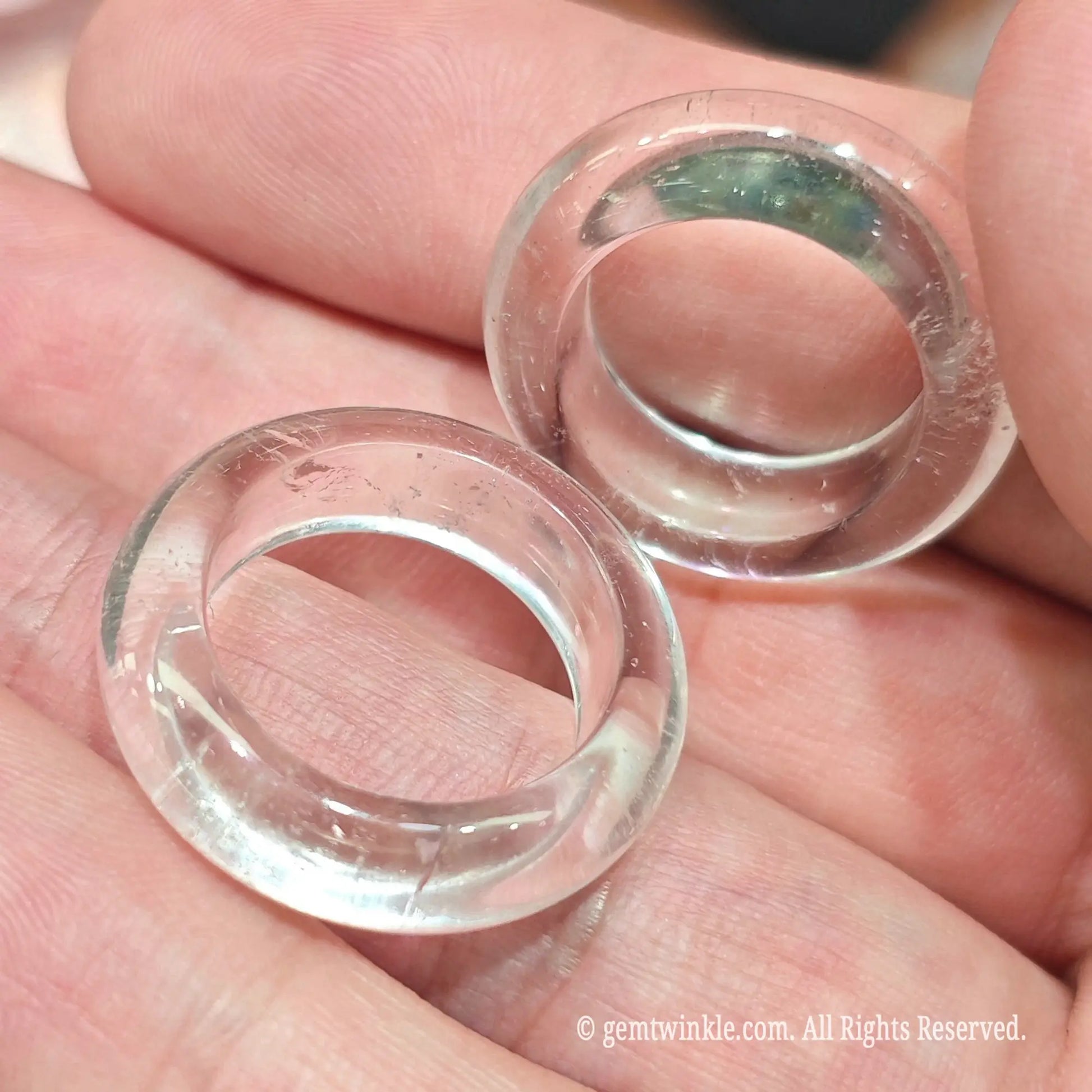 Angled view of clear quartz solid band rings held in hand showing smooth surface finish and light reflections