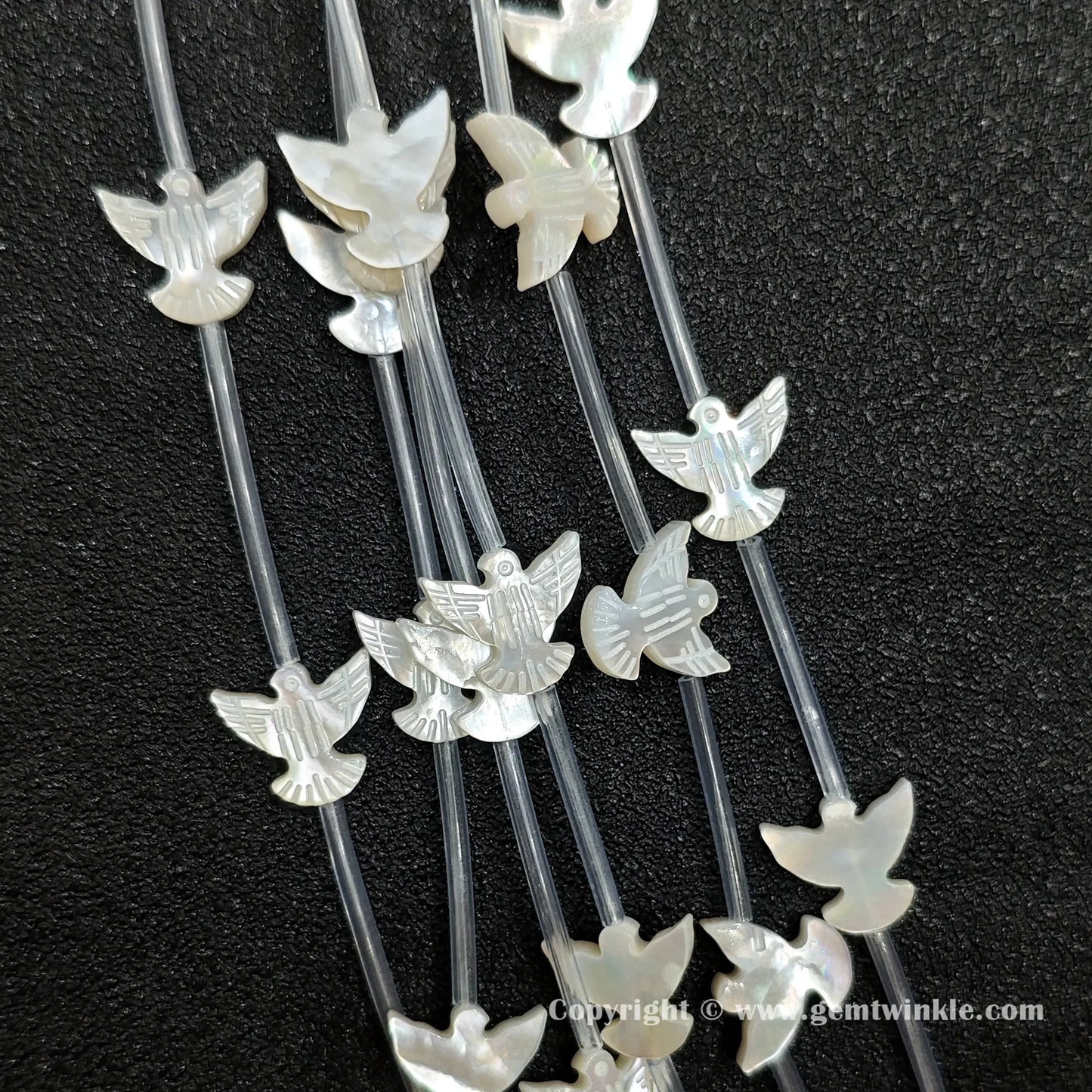 Close up view of carved white shell flying bird charms showing wing detail
