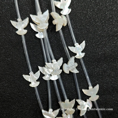 Close up view of carved white shell flying bird charms showing wing detail