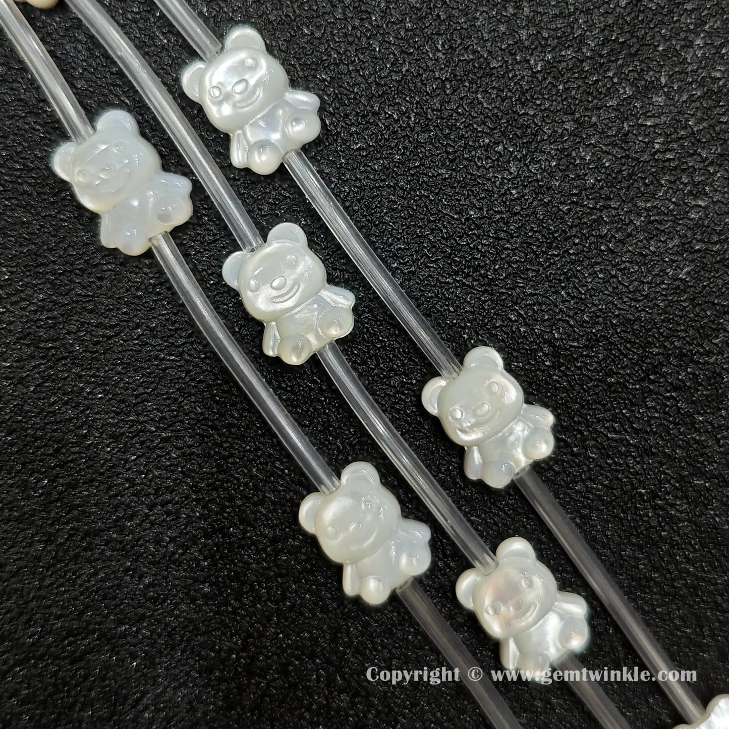 Close up view of carved white shell teddy bear charms showing relief detail