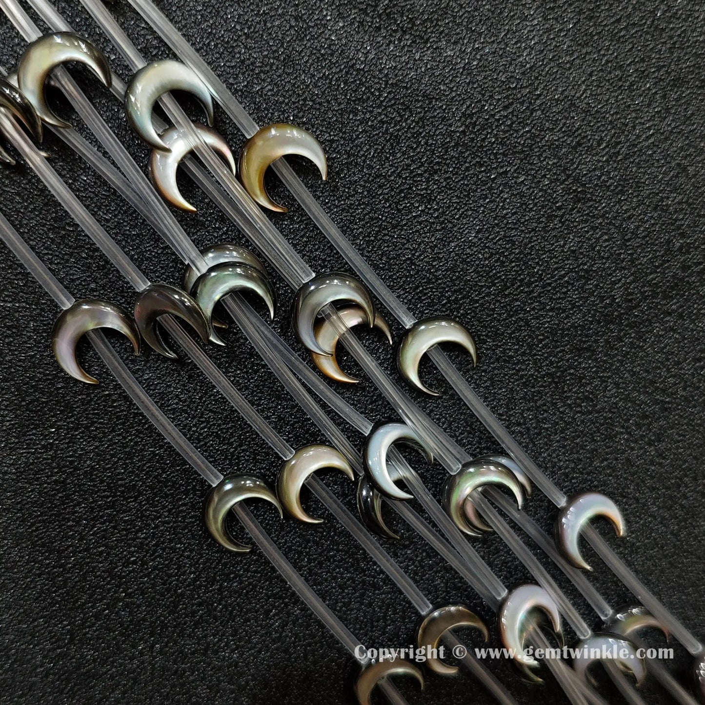 Close up view of dark shell machine carved crescent moon charms showing peacock luster