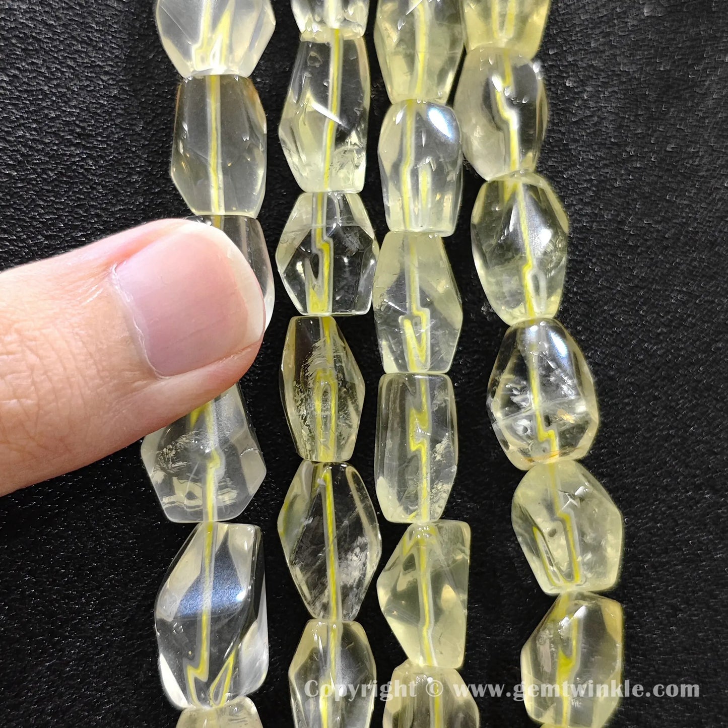 Hand holding 15mm lemon quartz faceted freeform barrel beads strand