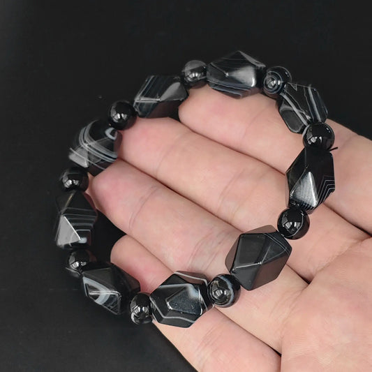 Color dyed black sardonyx 15mm faceted geometric bead bracelet held in hand showing white parallel silk banding
