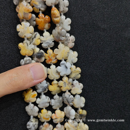 Close up view of crazy lace agate plum blossom carved beads held on fingers for quality preview