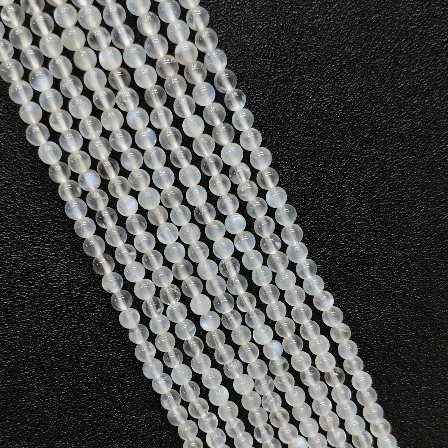 Macro closeup of creamy blue flash moonstone smooth round beads showing vivid optical blue sheen