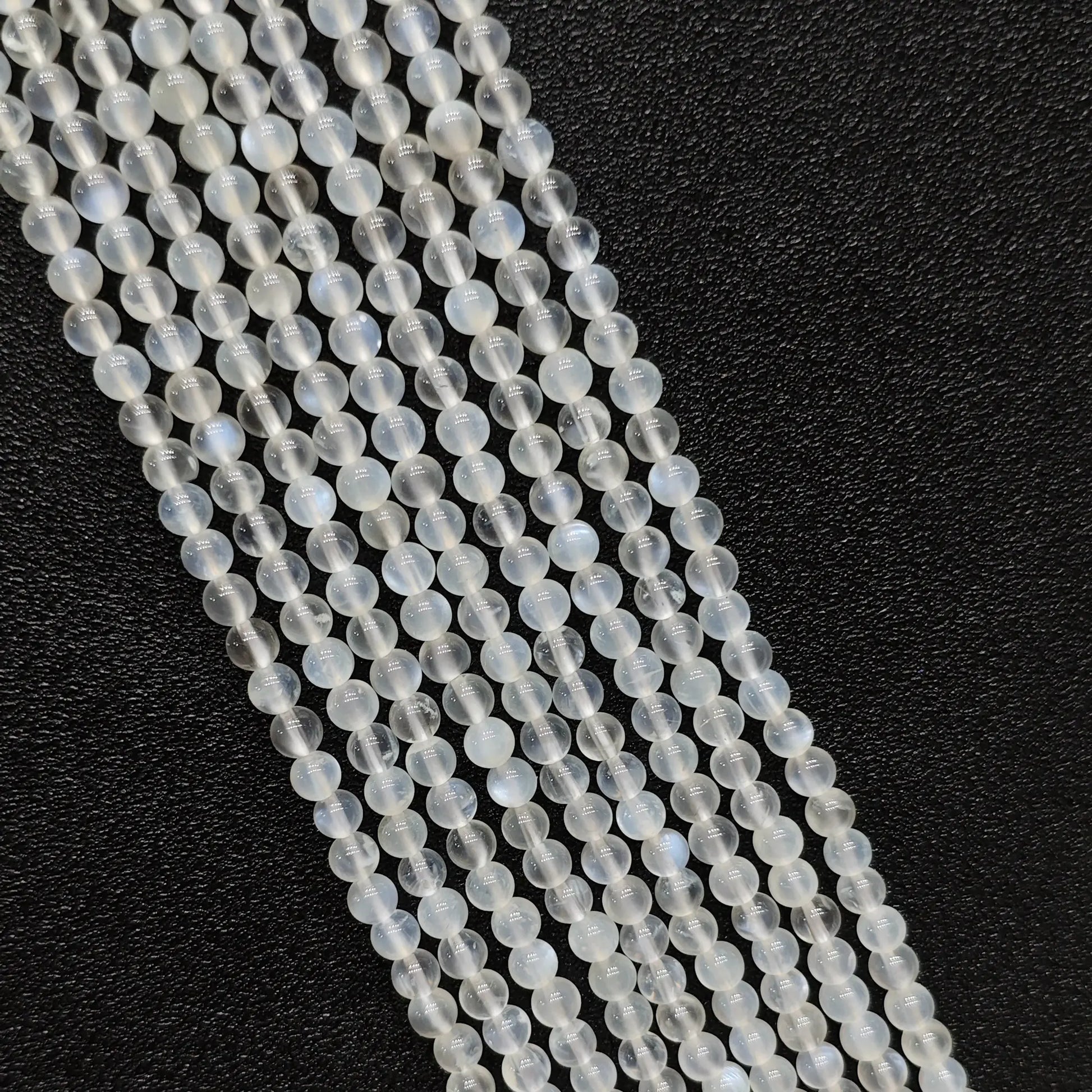 Macro closeup of creamy blue flash moonstone smooth round beads showing vivid optical blue sheen