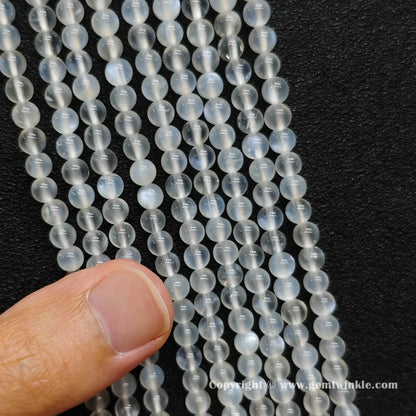 Close up view of creamy blue flash moonstone round beads inspected on hand for natural sheen preview