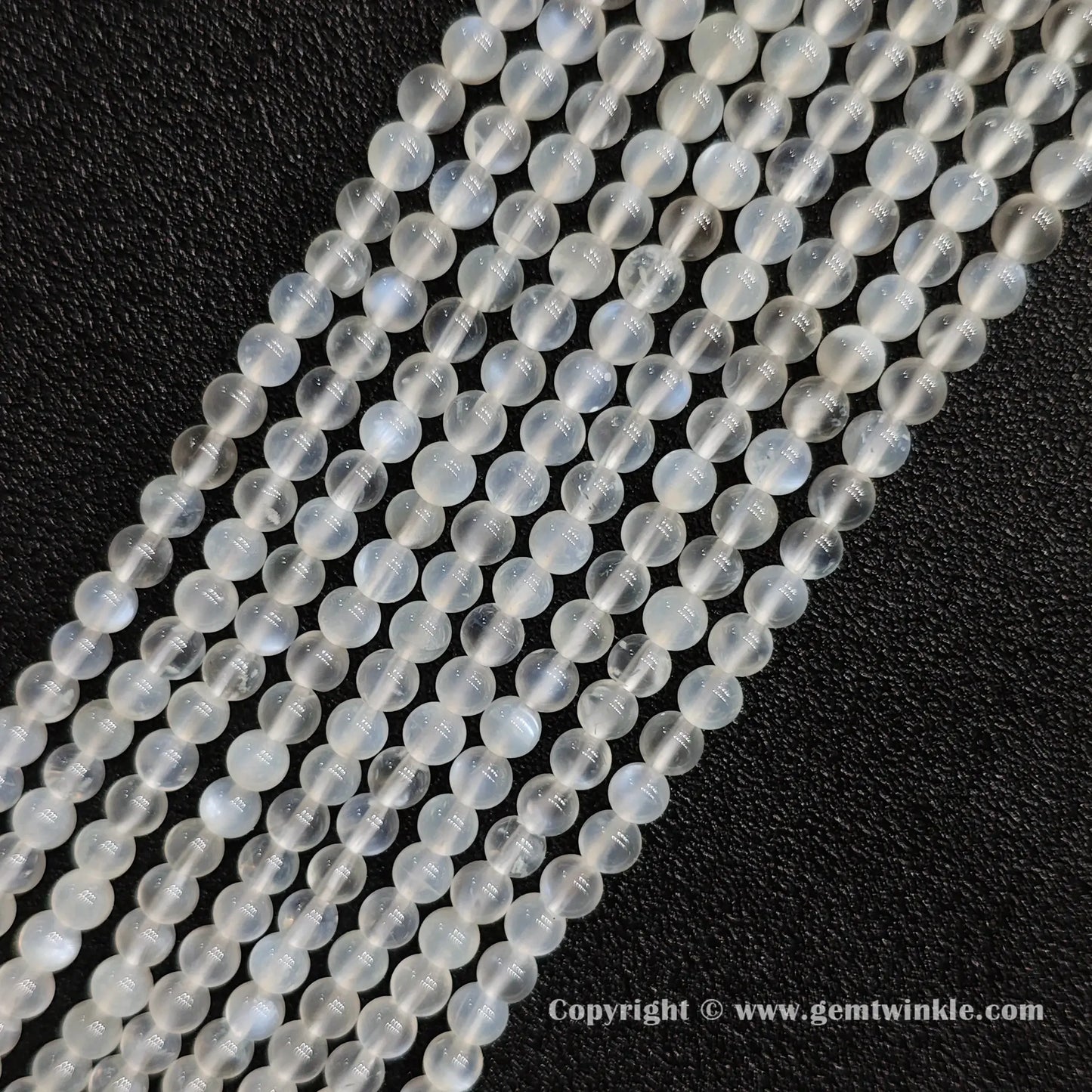 Angled view of creamy blue flash moonstone round bead strands laid parallel on dark textured surface