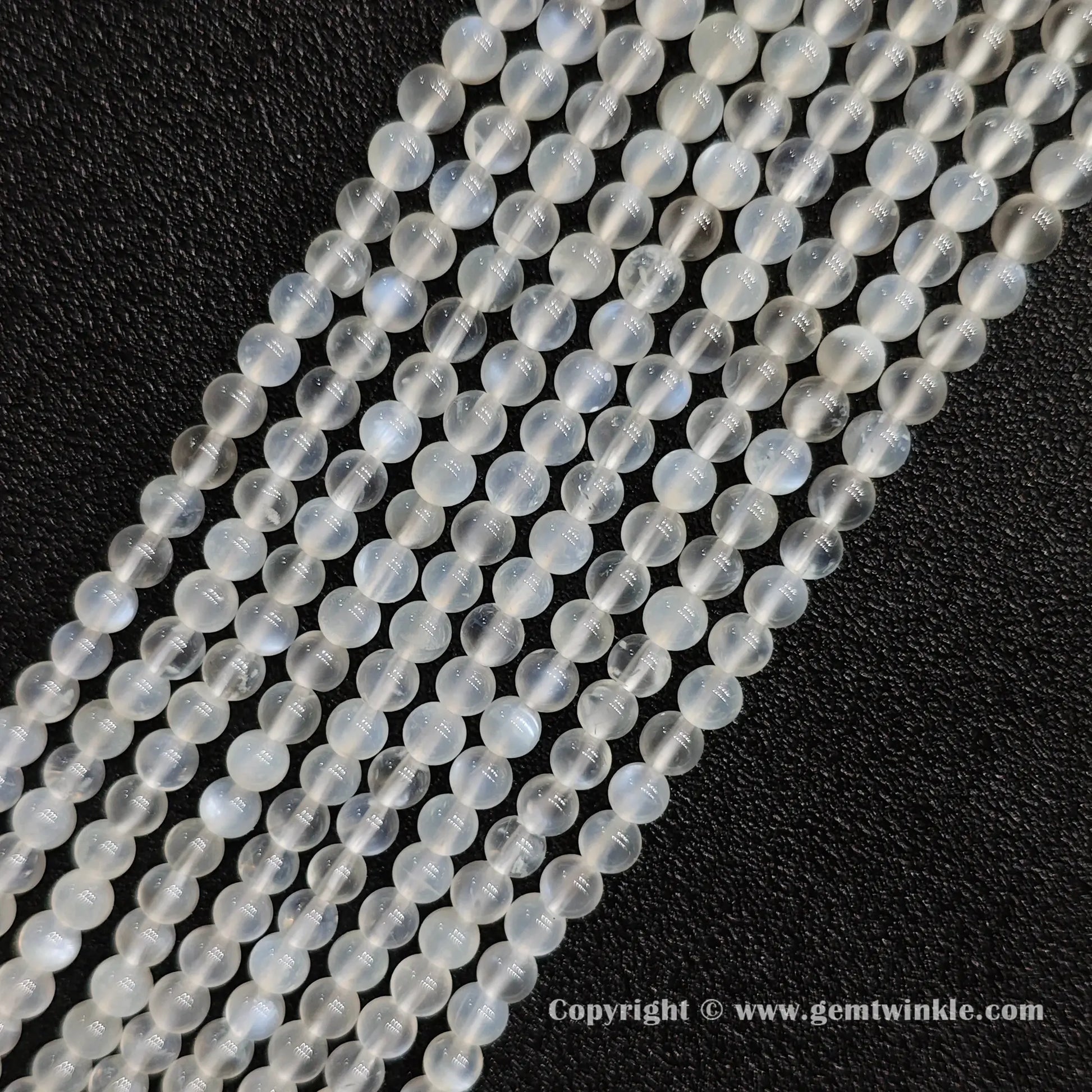 Angled view of creamy blue flash moonstone round bead strands laid parallel on dark textured surface