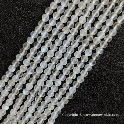 Angled view of creamy blue flash moonstone round bead strands laid parallel on dark textured surface