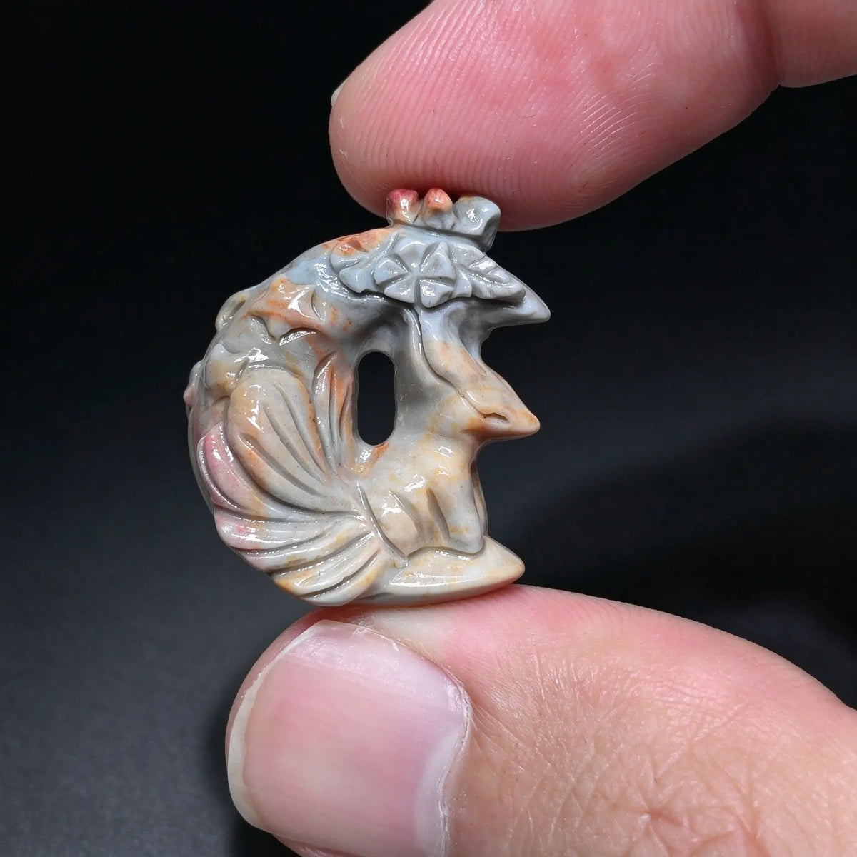 A tiny carved crescent moon fox figurine in natural sage gray and soft beige held gently between two fingertips
