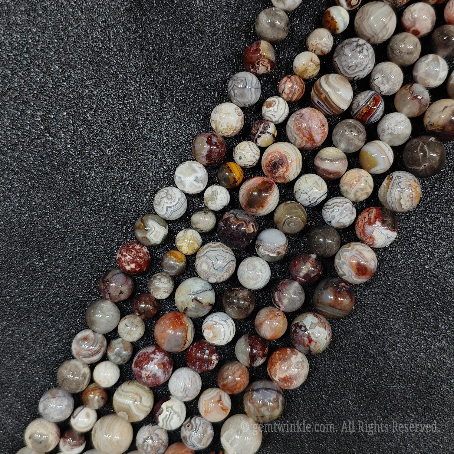 Close up view of natural un dyed crazy lace agate strands showing beautiful concentric ribbons and earthy grey red layers for handmade bracelet design