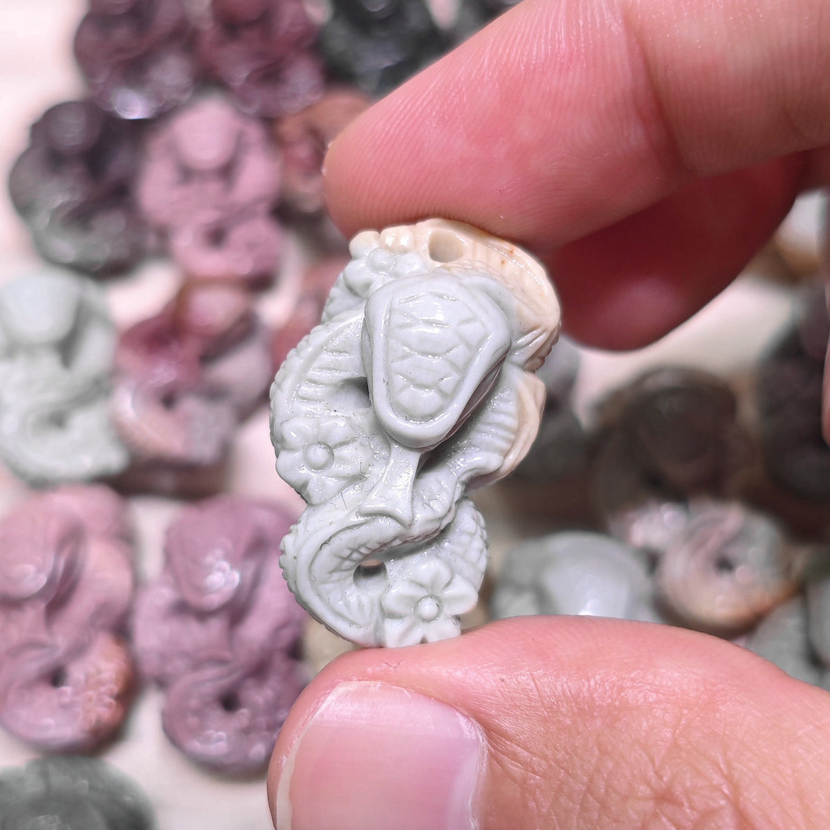 Fingers holding a small gray stone snake sculpture showing detailed cobra hood and floral textures