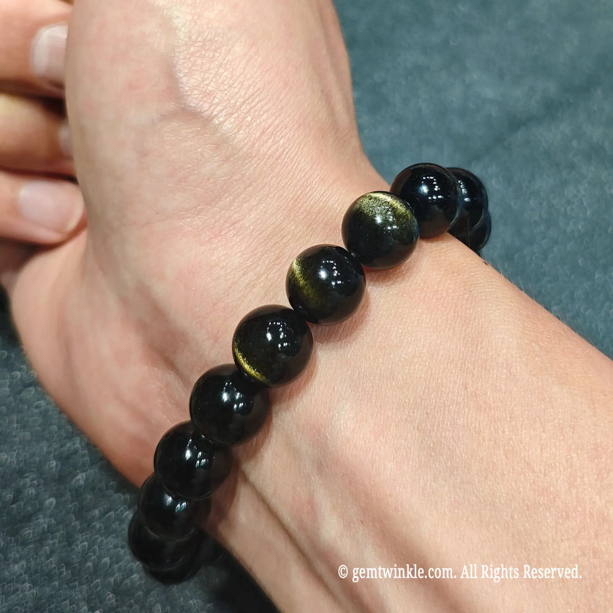 Hand worn view of a gold sheen obsidian bracelet demonstrating smooth polished beads with vibrant double light bands