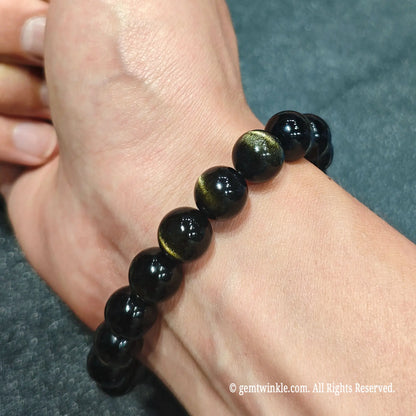 Hand worn view of a gold sheen obsidian bracelet demonstrating smooth polished beads with vibrant double light bands