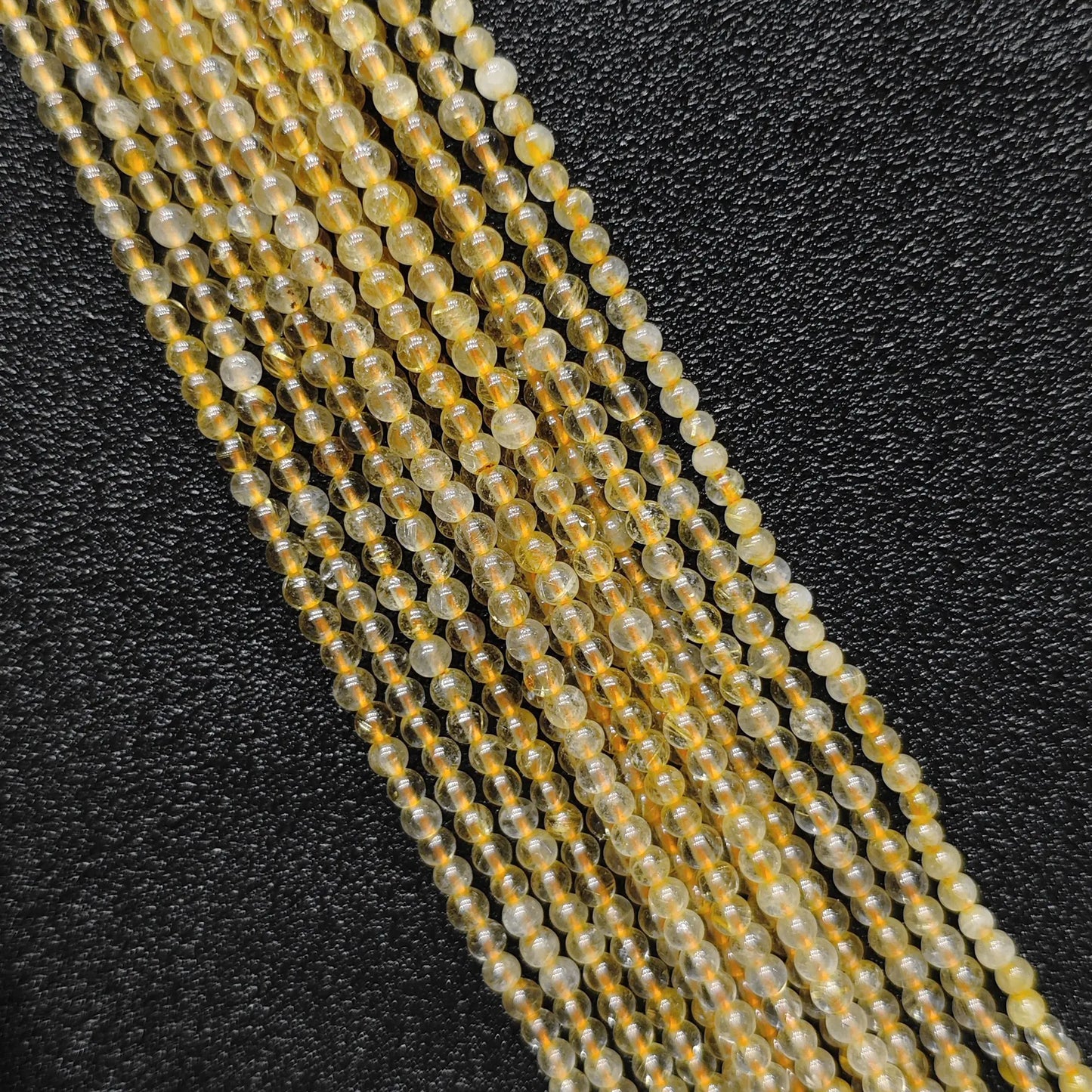 Close up view of 3mm dainty jewelry beads showcasing semi transparent natural gold rutilated quartz strands on a dark background