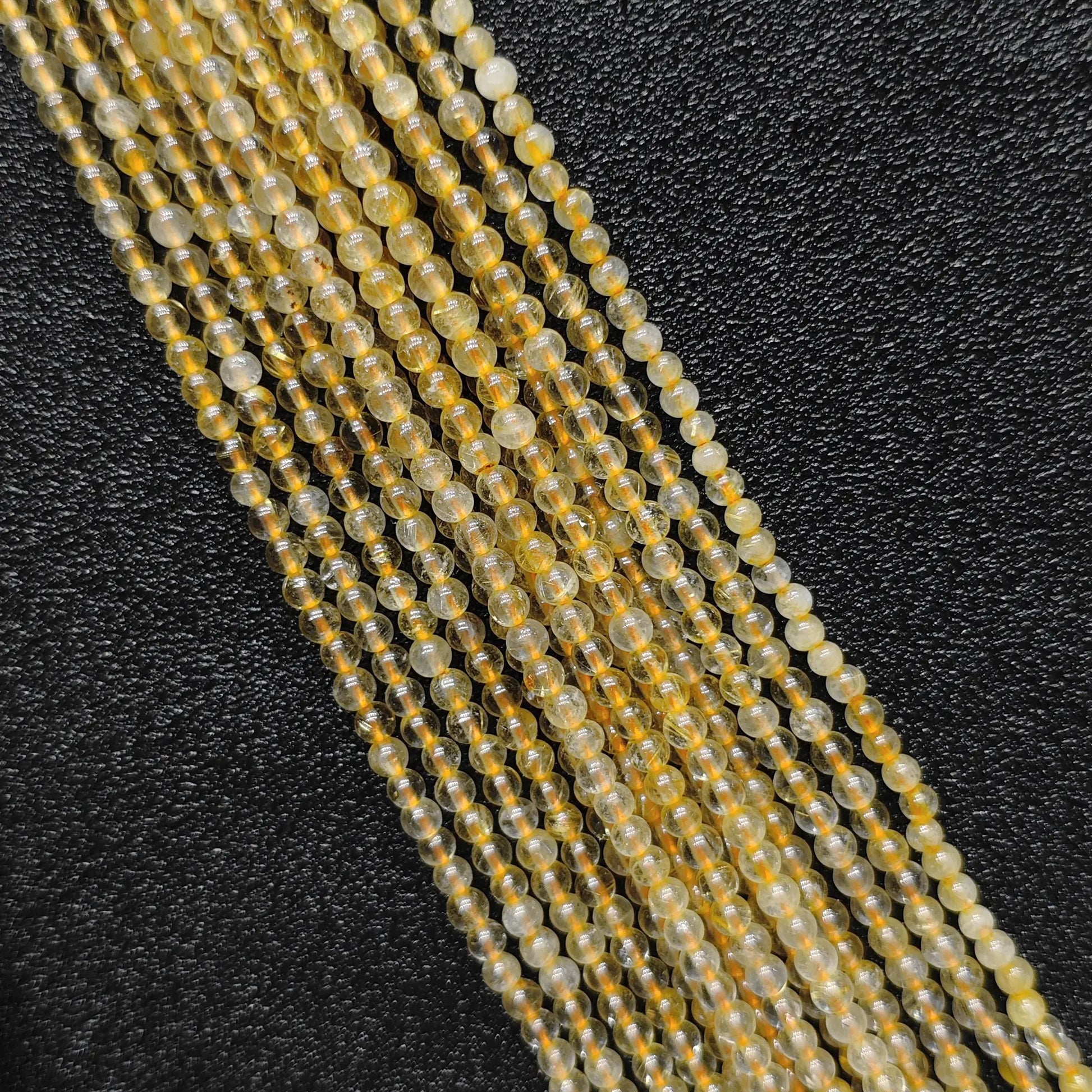 Close up view of 3mm dainty jewelry beads showcasing semi transparent natural gold rutilated quartz strands on a dark background