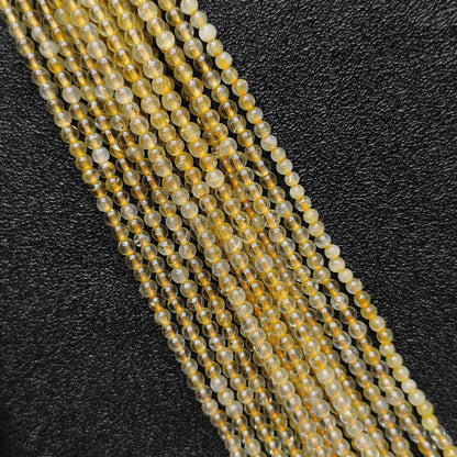 Close up view of 3mm dainty jewelry beads showcasing semi transparent natural gold rutilated quartz strands on a dark background