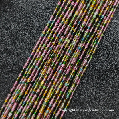 Multiple strands of dainty Grade B multi color tourmaline 2.5mm micro round beads on dark background