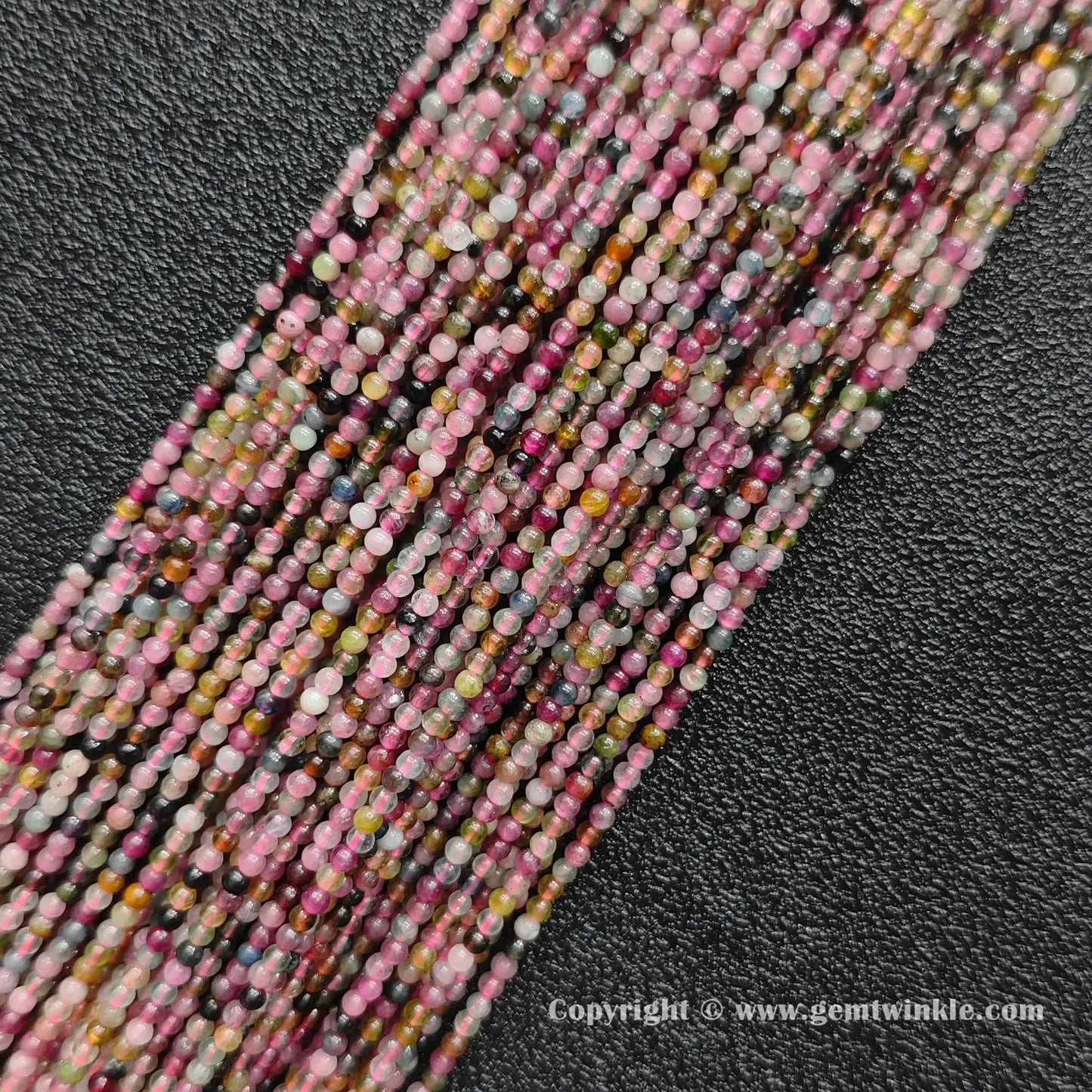 Multiple strands of dainty semi translucent multi color tourmaline 2mm mini beads on dark background
