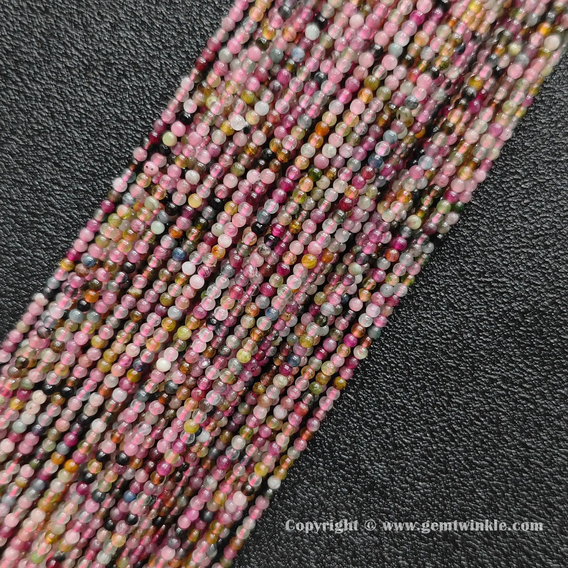 Multiple strands of dainty semi translucent multi color tourmaline 2mm mini beads on dark background