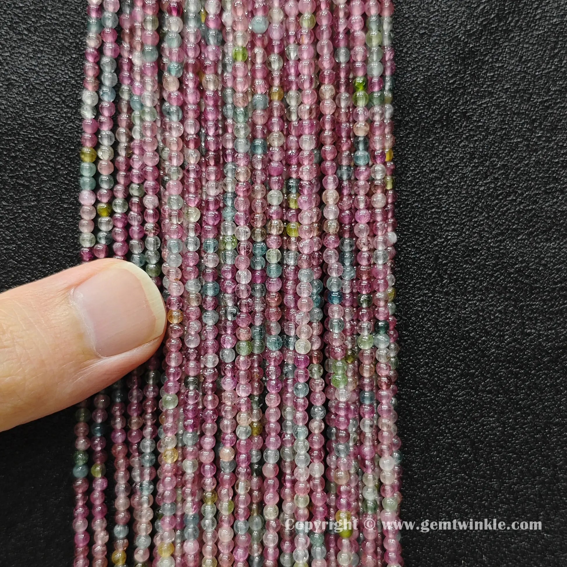 Vertical view of dainty light color tourmaline mini seed bead strands displaying polished luster