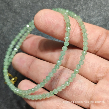 Coiled 3mm faceted green aventurine gemstone necklace held across fingers for layered necklace styling