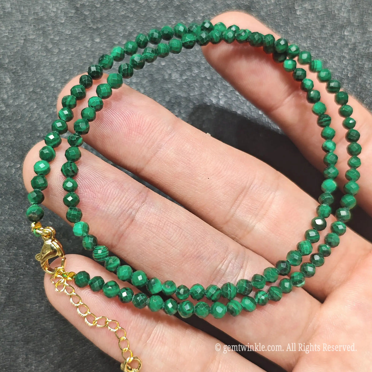 Coiled 3mm faceted malachite gemstone necklace held across fingers for layered jewelry displays