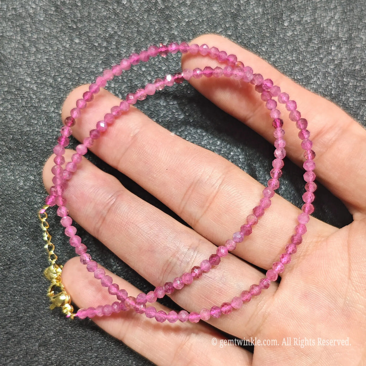 Coiled 3mm faceted pink tourmaline gemstone necklace held across fingers for layered jewelry displays